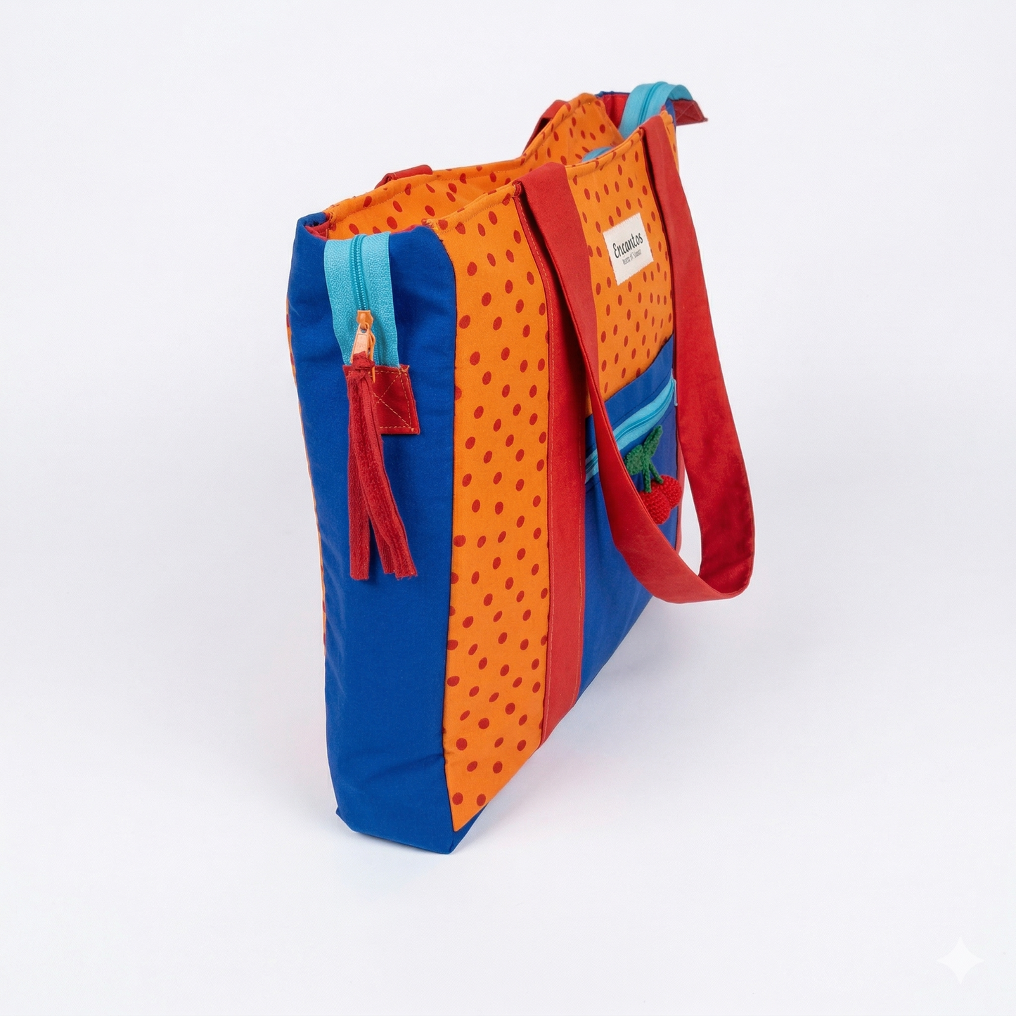 Bolsa Tote Cerezas — Encantos con diseño colorido en tonos naranja, azul y rojo, fabricada en tela resistente con detalles estampados y cierres visibles.