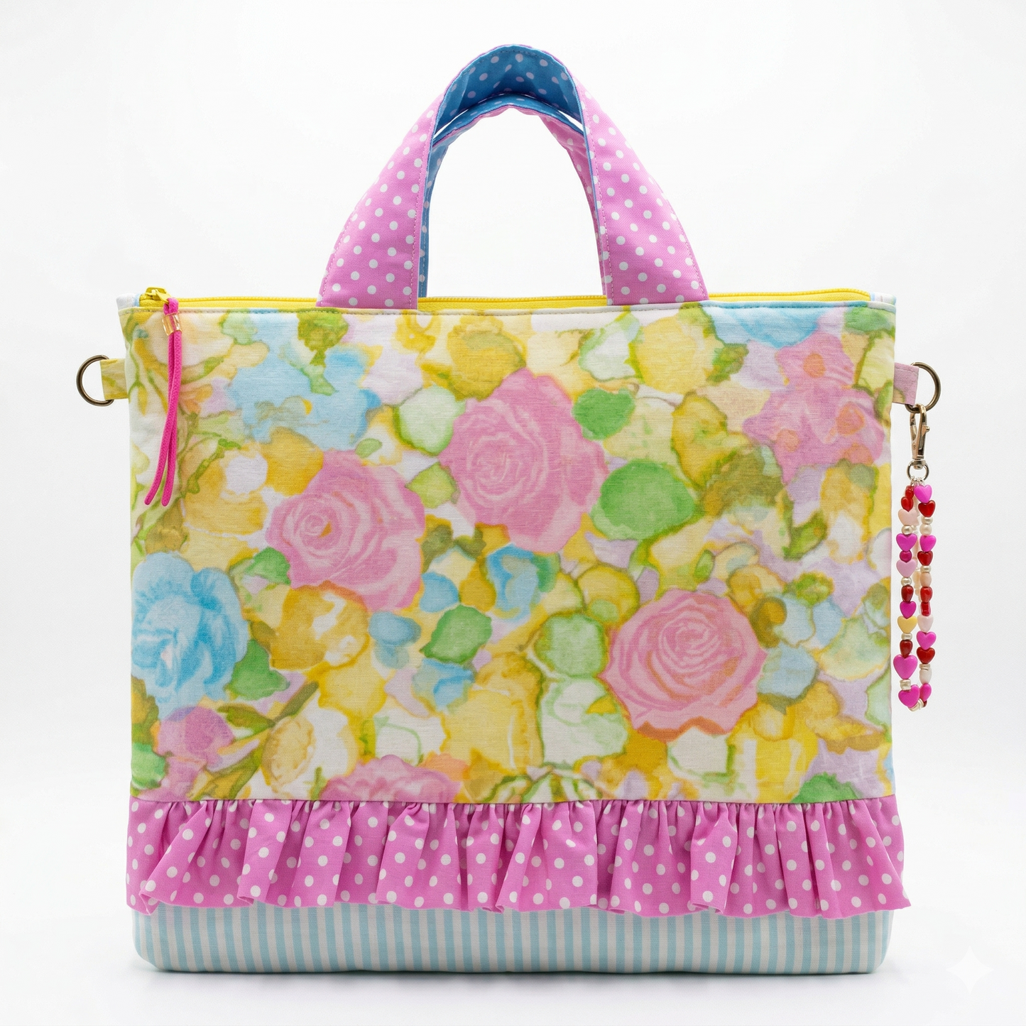 Bolso Tote Rosas Acuarela con estampado floral en tonos pastel, detalle de volante rosa con lunares blancos y asas a juego, accesorio colgante decorativo en forma de corazón.