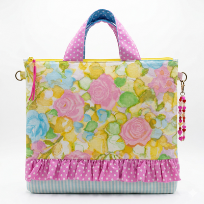 Bolso Tote Rosas Acuarela con estampado floral en tonos pastel, detalle de volante rosa con lunares blancos y asas a juego, accesorio colgante decorativo en forma de corazón.