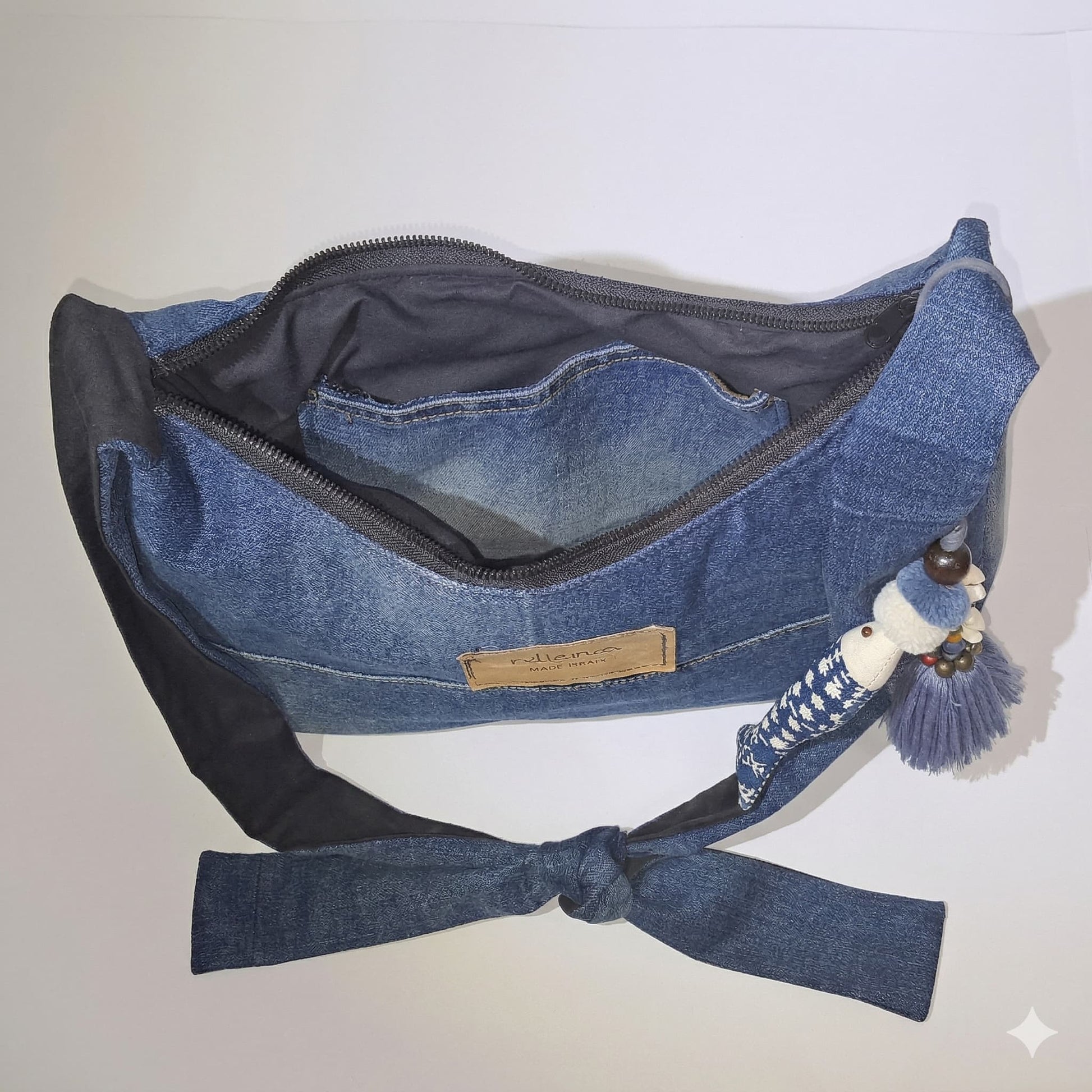 Bolso Denim con Lazo y Borlas abierto que muestra su interior forrado y diseño en mezclilla azul con detalles en lazo y borlas decorativas.