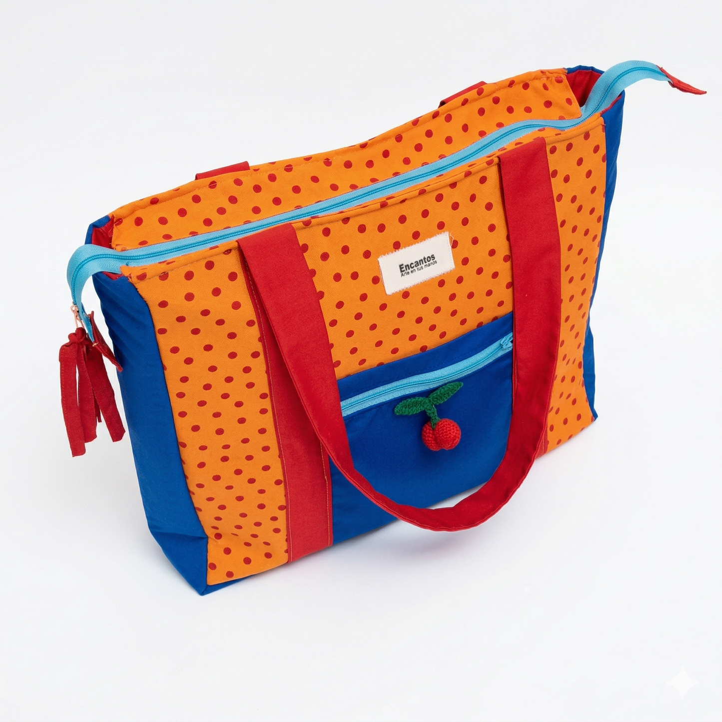 Bolsa Tote Cerezas — Encantos con diseño en naranja y azul, detalles en rojo, cierre celeste y pequeño adorno de cerezas tejido en el bolsillo frontal.