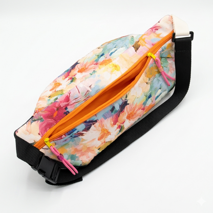 Riñonera Floral Denim con diseño de flores coloridas, cierre naranja y correa negra ajustable, ideal para llevar objetos personales con estilo y comodidad.