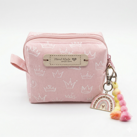 Neceser Cube Rosa Hand Made with Love de tela rosa con estampado de coronas blancas, cremallera y llavero con decoración de arcoíris y pompones.