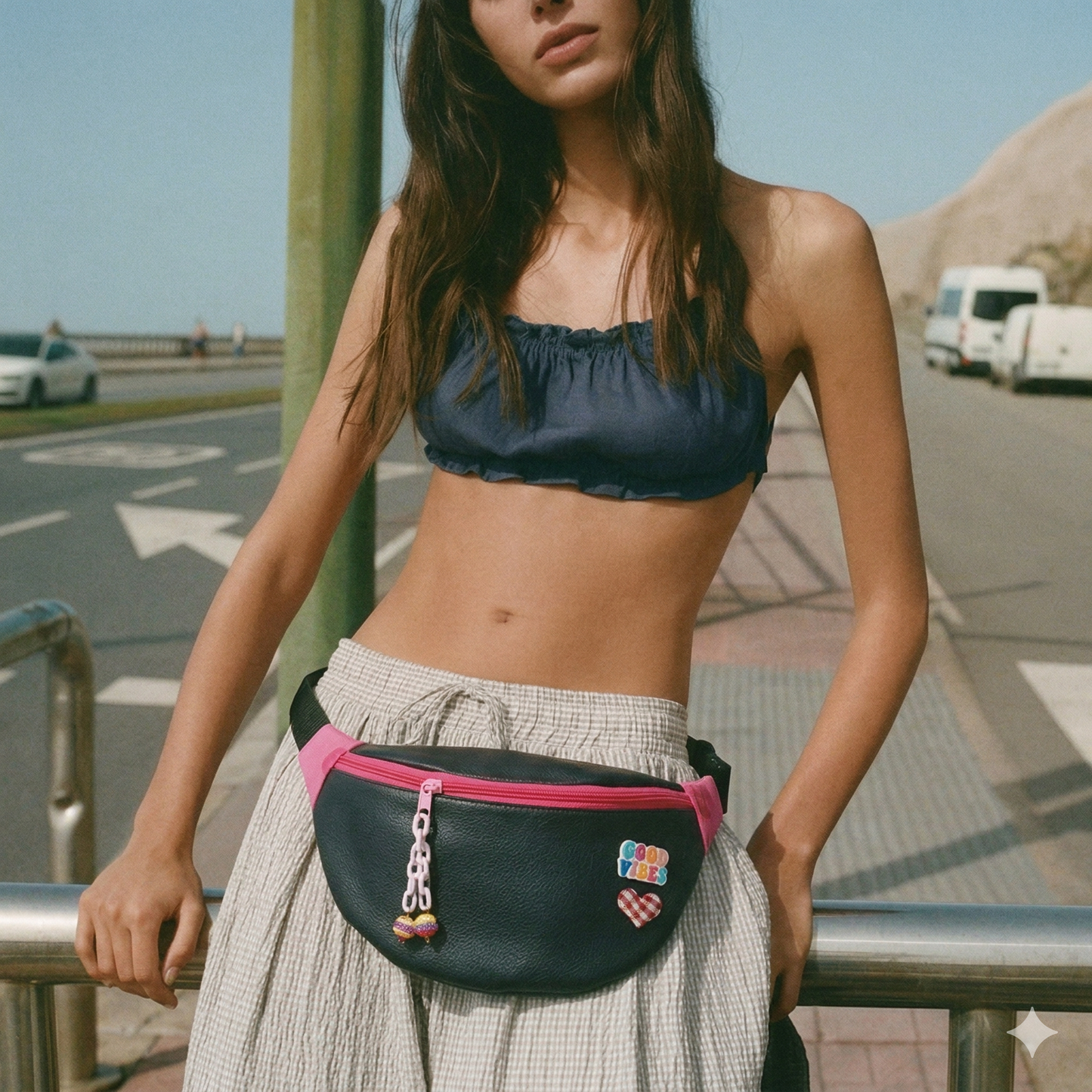 Mujer con top azul oscuro y falda clara usando una Riñonera Corazón Vichy Negro & Rosa | Encantos en la cintura, con cierre rosa y detalles decorativos.