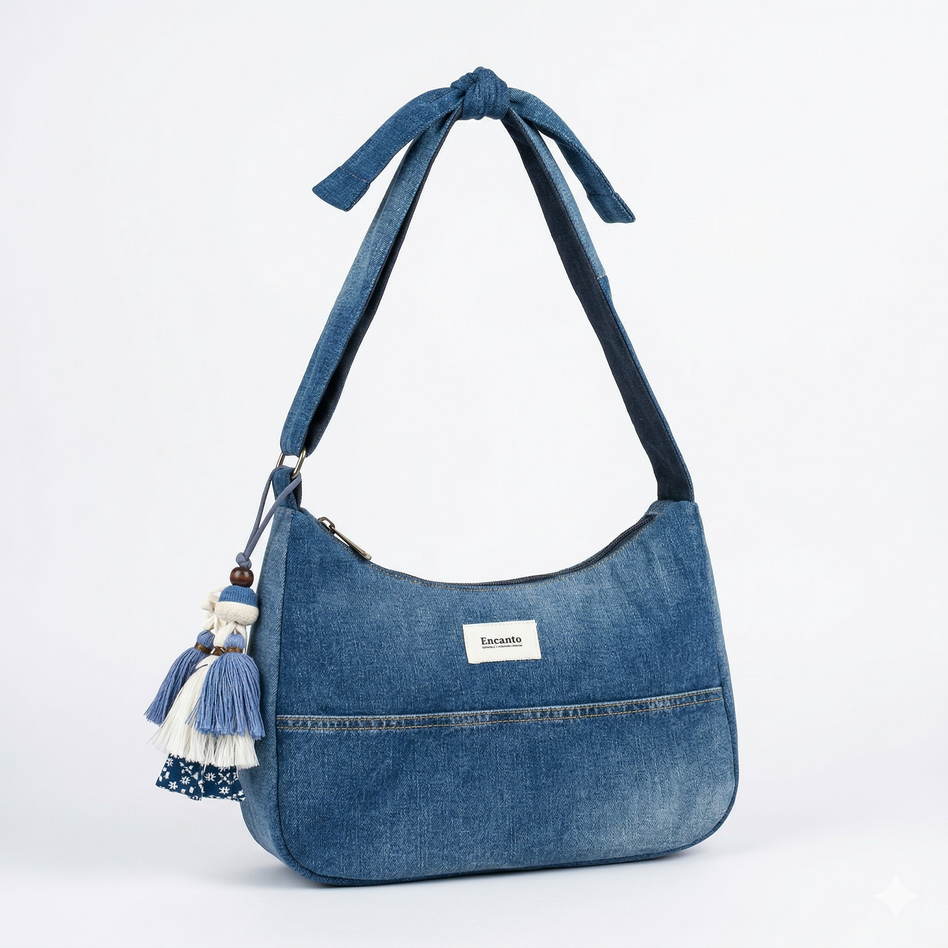 Bolso Denim con Lazo y Borlas hecho de mezclilla azul con detalle de lazo en la correa y borlas decorativas colgantes en un lado.