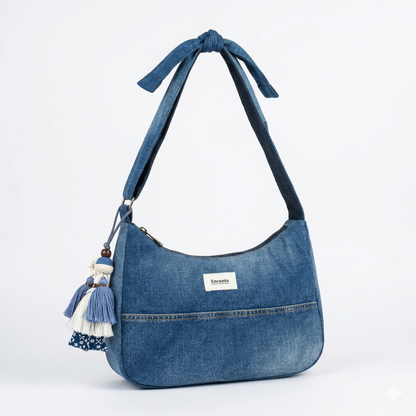 Bolso Denim con Lazo y Borlas hecho de mezclilla azul con detalle de lazo en la correa y borlas decorativas colgantes en un lado.
