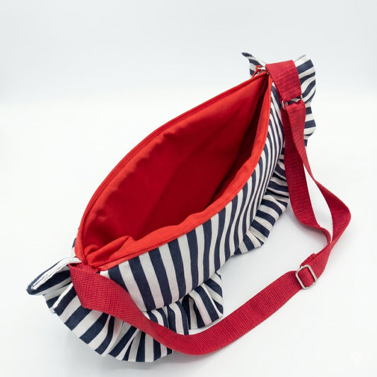 Interior del bolso HALF MOON de Encantos abierto, mostrando forro rojo intenso, cremallera roja y asa regulable. Tela exterior de rayas azul marino y blanco con volante artesanal


