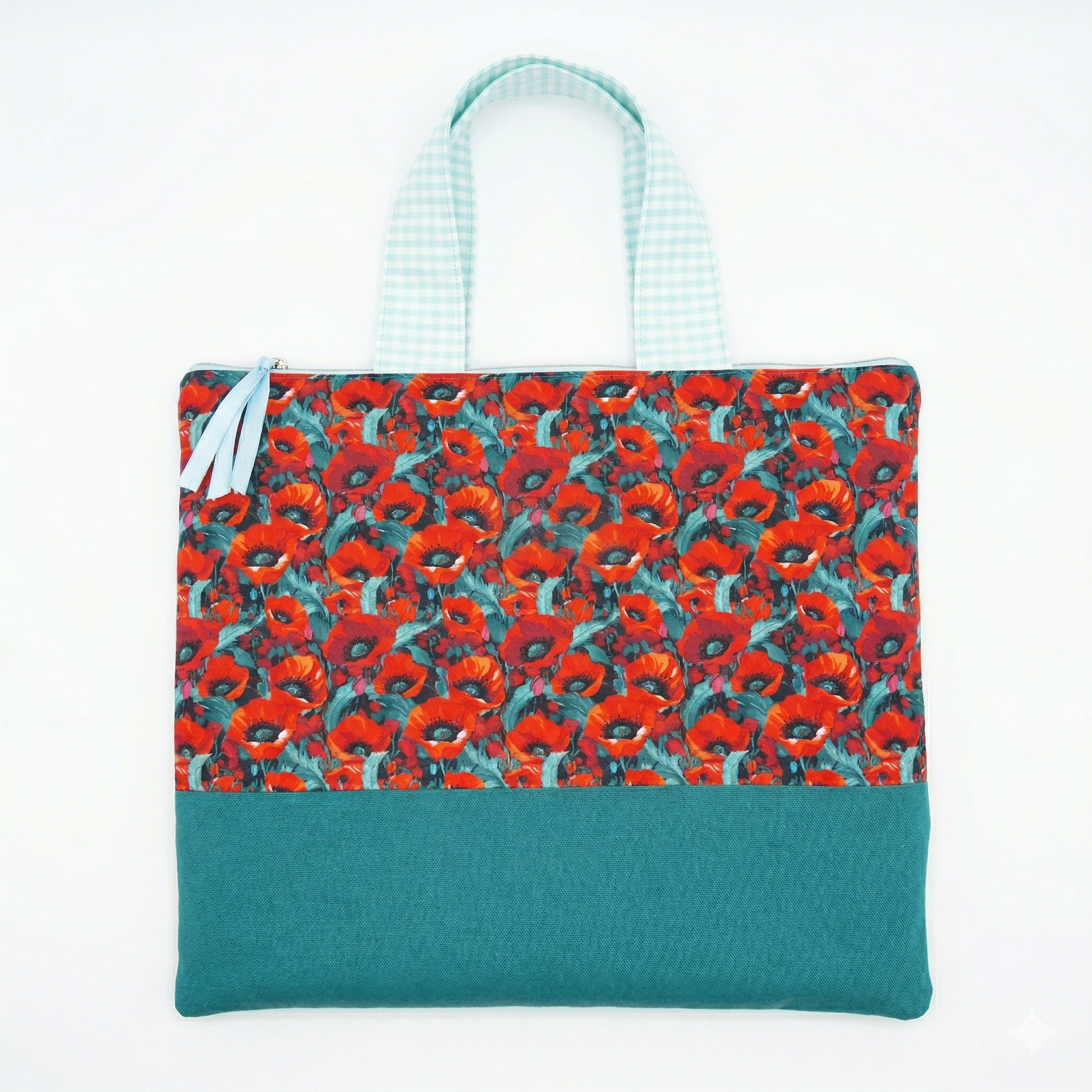 Bolso Cuquito con Amapolas y Volante en tonos rojos y verdes con asa de tela a cuadros celestes, diseño floral vibrante y cierre con cintas decorativas.