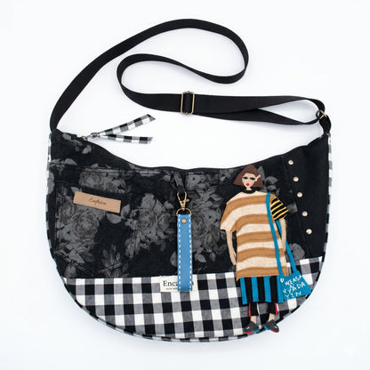Bolso Luna Flores & Vichy Negro — Encantos con diseño mixto de flores y cuadros vichy en negro, con detalle artesanal de figura femenina y correa ajustable negra.