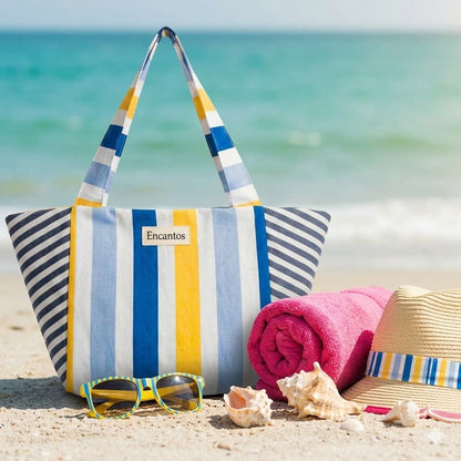 Bolso playero Encantos de rayas azul y amarillo en la arena con toalla rosa, sombrero y conchas